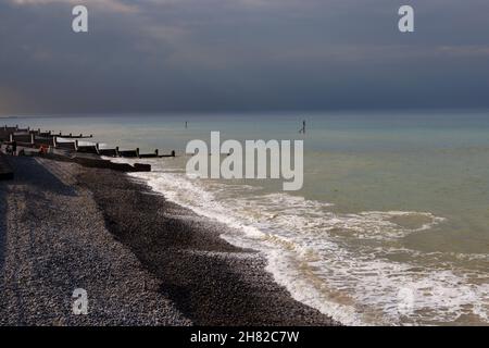 Les vagues se brisent sur la rive de la plage de galets par des groynes en bois typiques à Sheringham, sur la côte nord de Norfolk, avec à l'approche de mauvais temps Banque D'Images