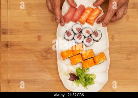 Les mains du chef préparent un plateau blanc de sushis et de maki de thon rouge et de roulades de californie uramaki avec des œufs de macago et un délicieux nigiri de norvégien Banque D'Images