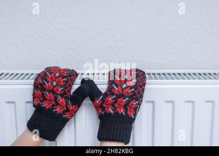 Mains dans les mitaines sur le radiateur.Basse température dans les maisons en hiver. Banque D'Images