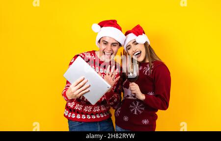 jeune couple latin ayant des appels vidéo de noël à l'aide d'une tablette numérique ou d'un pavé tactile sur un fond jaune Banque D'Images