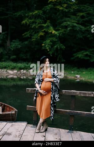 La femme enceinte s'appuie sur la rampe de la jetée avec des bateaux sur le lac Banque D'Images