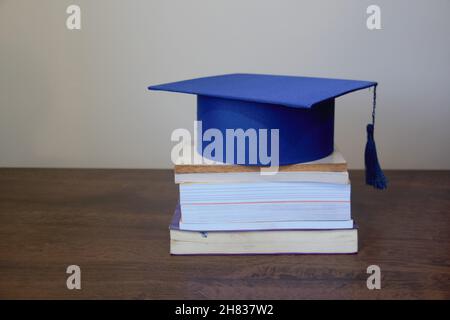 Chapeau de graduation, isolé, au-dessus d'une pile de livres sur une table en bois avec fond blanc. Banque D'Images