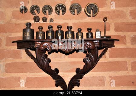 Des poids anciens, sur un panneau latéral en bois, sur un mur rustique en brique. Banque D'Images