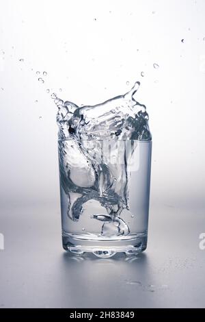 Verre d'eau avec éclaboussures sur une surface gris clair et un fond blanc. Banque D'Images