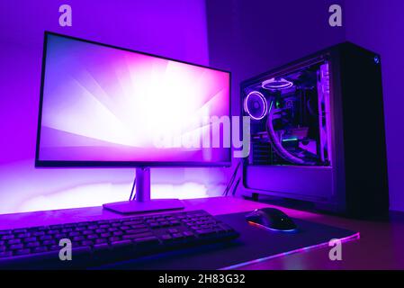 Configuration moderne de l'ordinateur de jeu avec écran, boîtier de refroidissement de l'eau, clavier, souris sur tapis de jeu.Lumière LED violette en arrière-plan Banque D'Images