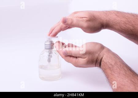 Gros plan d'un homme mettant du gel désinfectant à base d'alcool sur ses mains contre un fond blanc Banque D'Images