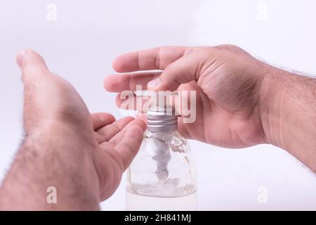 Gros plan d'un homme mettant du gel désinfectant à base d'alcool sur ses mains contre un fond blanc Banque D'Images