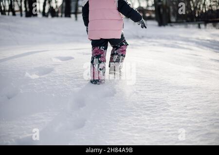 Empreintes des pieds des enfants dans la neige.Vue arrière de l'enfant dans des vêtements chauds d'hiver marchant dans des déneigeuses et jouant dans les bois après une tempête de neige intense Banque D'Images