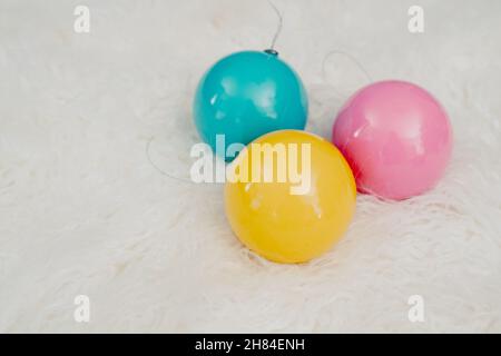 Grandes ampoules de Noël en plastique bleu, jaune, rose sur fond de fourrure blanche Banque D'Images