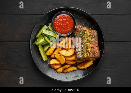 Vue de dessus des côtes de bœuf rôties avec des quartiers de pommes de terre et du concombre mariné sur une assiette Banque D'Images