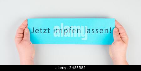 Se faire vacciner maintenant est debout en langue allemande sur le papier, Covid-19 vaccination, mains tenant le message Banque D'Images