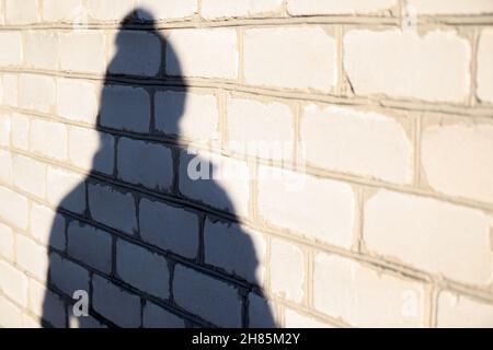 Recentrer l'ombre de la personne dans la casquette d'hiver sur le mur de brique blanche.Femmes légères et d'ombre.Silhouette féminine.Les gens ombres avec réflexion sur le ho Banque D'Images