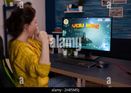 Une joueuse joueuse gagnante excitée gagne des jeux vidéo de tir spatial lors d'un tournoi de jeu en ligne dans le salon à la maison.Joueur effectuant des compétitions de cybersport.Victoire des jeux vidéo Banque D'Images