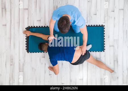 Vue du dessus d'un thérapeute aidant un patient masculin tout en étirant sa jambe à l'hôpital.Photo de haute qualité Banque D'Images