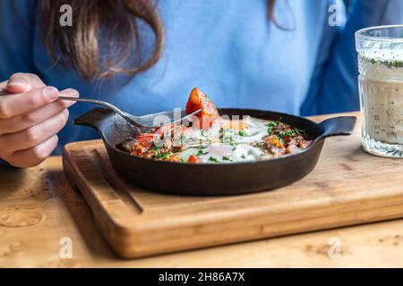 En gros plan, une femme dans un café dines sur le shakshuka traditionnel. Banque D'Images