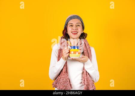 jeune femme hispanique, avec une tasse en argile de café ou punch de fruits pour l'hiver sur fond jaune en amérique latine Banque D'Images