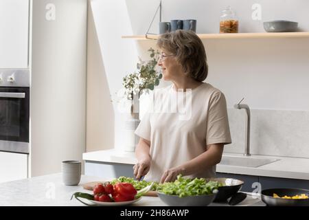 Bonne femme mûre faisant de la salade dans la cuisine Banque D'Images