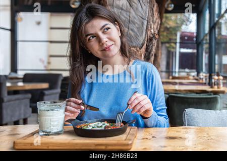 Une jeune femme dans un café dines sur le shakshuka traditionnel et ayran. Banque D'Images