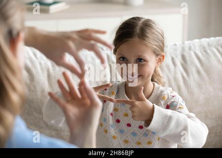 Petite fille souriante apprenant la langue des signes avec maman. Banque D'Images