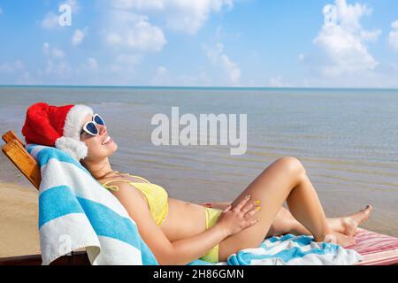 belle jeune femme en chapeau de père noël et lunettes de soleil se détendant sur chaise longue Banque D'Images