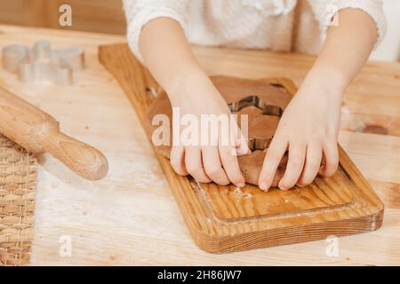 les mains des enfants sculpte des biscuits sur la pâte de pain d'épice provenant de figurines.Fille préparant des biscuits de noël sur une table en bois Banque D'Images