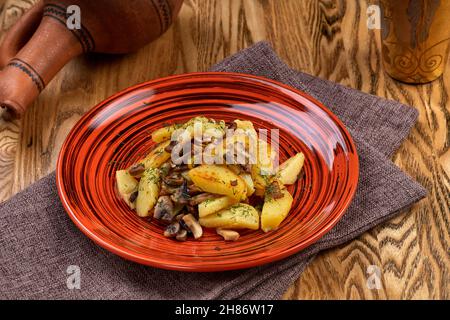 Quartiers de pommes de terre cuits avec champignons dans un plat rouge, vue en angle. Banque D'Images