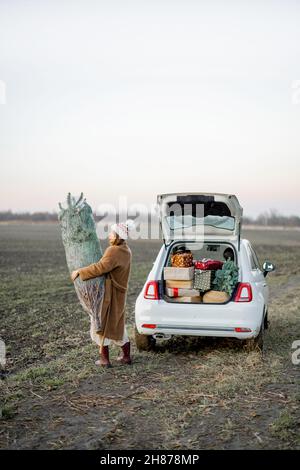 Femme qui va avec l'arbre de Noël près de la voiture sur la nature Banque D'Images