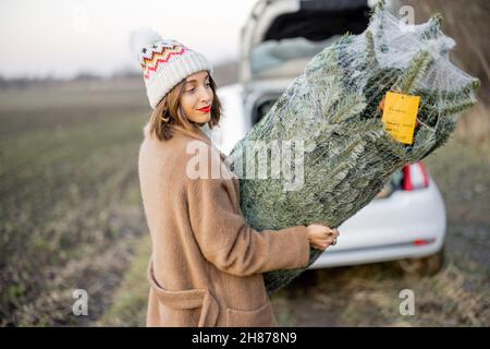 Femme qui va avec l'arbre de Noël près de la voiture sur la nature Banque D'Images