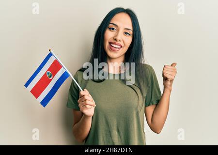 Jeune fille hispanique portant le drapeau du costa rica pointant le pouce vers le côté souriant heureux avec la bouche ouverte Banque D'Images