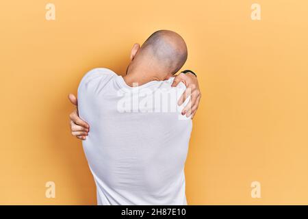 Jeune homme bald portant un t-shirt blanc décontracté se embrassant heureux et positif de l'arrière-plan. Amour de soi et d'auto-soins Banque D'Images