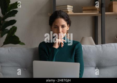 Une femme hispanique attentionnée utilise un ordinateur portable sur le canapé à la maison Banque D'Images