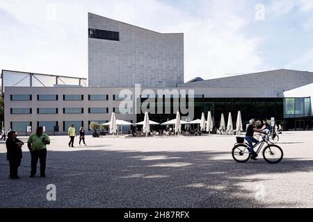 Vue sur la Festspielhaus Bregenz avec un café en plein air avec des tables, des chaises et des parasols. Sur la piste et un cycliste. Banque D'Images