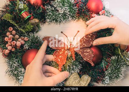 Couronne de Noël à la porte d'entrée.Vue de dessus des mains de femmes décorant la couronne de Noël avec des boules rouges avec papillon en forme de jouet de Noël.L'Avent de la famille Banque D'Images
