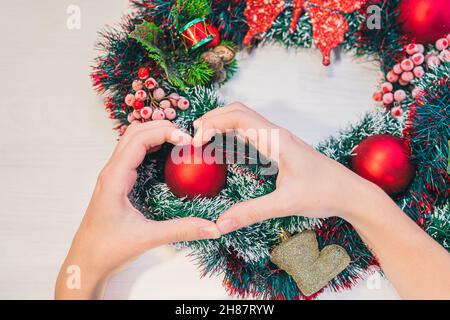 Couronne de Noël sur fond de bois.Les mains des femmes montrent le symbole du coeur sur le fond de la couronne de Noël avec des boules rouges. Banque D'Images