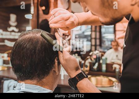 Coiffeur professionnel effectue une coupe de cheveux pour les hommes. Le client homme est assis dans une chaise de coiffeur professionnelle, et le coiffeur fait une coupe de cheveux. Banque D'Images