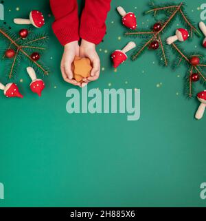 Pain d'épice dans les mains d'un enfant sur fond vert avec des jouets de noël Banque D'Images