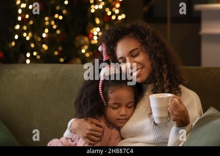 Petite fille afro-américaine embrassant sa mère avec une tasse de chocolat chaud la veille de Noël Banque D'Images