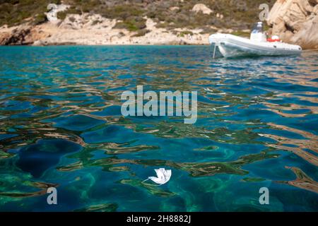 Pollution par masque médical jetable sur la plage par la mer due à une pandémie de coronavirus. Banque D'Images