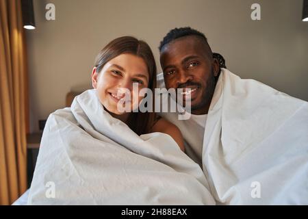 Joyeux jeune couple de course mixte assis au lit Banque D'Images