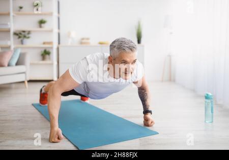 Homme fort senior faisant de l'entraînement de force, faisant des push-up sur tapis de sport, l'exercice à la maison, l'espace de copie Banque D'Images