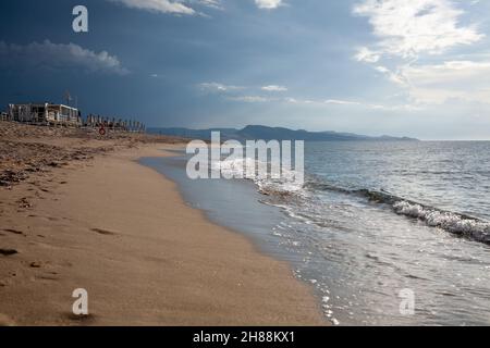 Plage de sable vide, perchée par les vagues d'eau de mer avant la tempête, au coucher du soleil. Banque D'Images