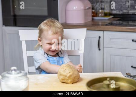 Le petit garçon se réjouit de la pâte finie pour des pâtisseries sucrées dans la cuisine. Banque D'Images