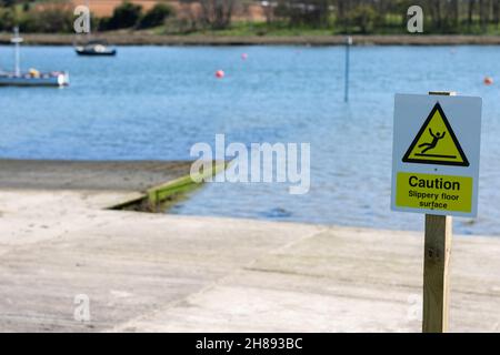 Panneau d'avertissement pour une surface de sol glissante sur une jetée au bord d'une rivière.Le signe blanc et jaune est également doté d'un symbole d'image clair indiquant que l'homme glisse et tombe sur le dessus. Banque D'Images