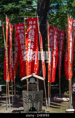 Sanctuaire à l'entrée du Zenizuka Mizo-do Hall dédié à la prospérité dans les affaires, au complexe de temples bouddhistes Sensoji à Asakusa, Tokyo, Japon.Les bannières rouges appelées bannières nobori entourent un lavabo en pierre pour la purification. Banque D'Images