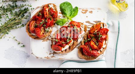 Sandwichs avec tomates cerises cuites au four et fromage cottage, thym, ail et herbes sur un fond ancien et léger d'époque.Vue de dessus. Banque D'Images