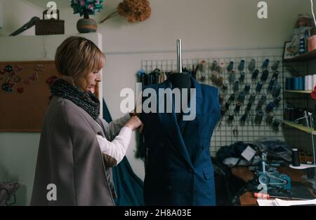 Une couturière féminine superpose manuellement un costume sur un mannequin dans un atelier de couture. Banque D'Images