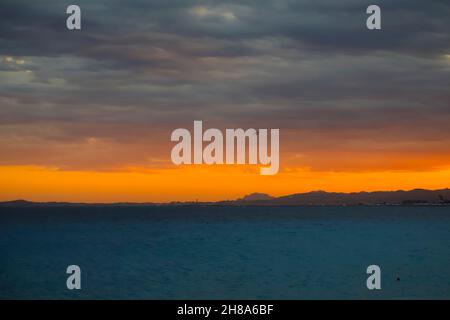 Sur la mer Méditerranée à Nice un coucher de soleil est venu.Au loin, vous pouvez voir les collines et silhouettes de la ville. Banque D'Images