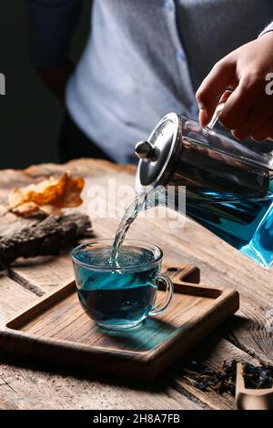 Femme versant le thé de fleur de pois papillons de la théière dans une tasse sur la table Banque D'Images