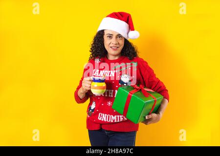 latino noël femme d'âge moyen avec une tasse d'argile de punch de fruit sur fond jaune au mexique amérique latine Banque D'Images