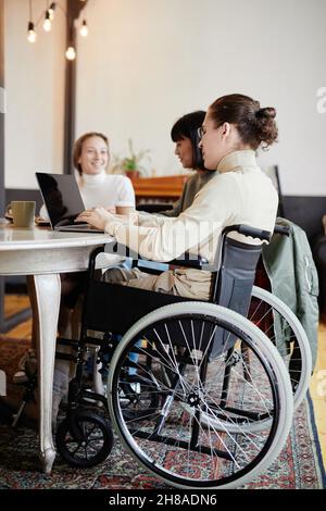 Étudiant handicapé assis en fauteuil roulant et étudiant sur un ordinateur portable tout en étant assis à la table avec ses camarades de classe Banque D'Images